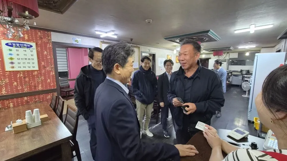 한 회원이 웃으며 카드를 내밀고 주변 회원들이 웃고 있는 장면